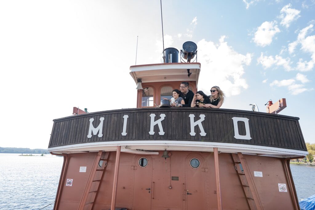 Kaksi aikuista ja kaksi lasta seisovat vanhan laivan yläkannella. Edessä näkyy laivan nimi Mikko.