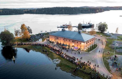 Keskellä museon vanha tiilinen rakennus ja ympärillä syksyinen järvimaisema vanhoine museolaivoineen. Rakennuksen etupihalla on suuret joukot ihmisiä sekä muutama myyntikoju.